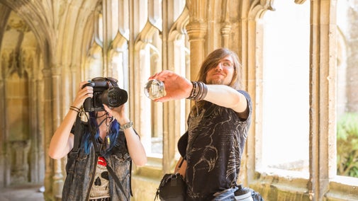 Two people take photos in the Cloister at Lacock Abbey, one uses a digital camera whilst the other holds a glass prism for the camera to view the scene through.